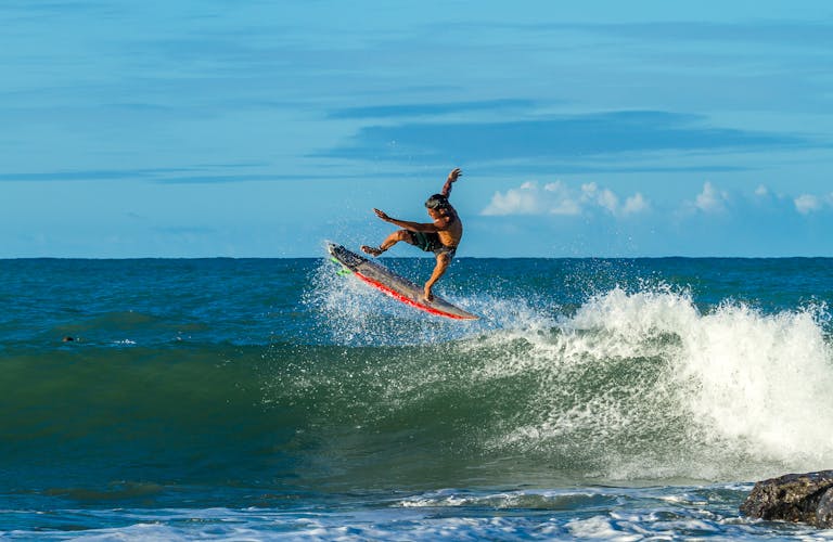 Surfer performing an aerial maneuver on a sunny day, showcasing dynamic surfing skills.